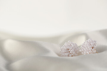 Beautiful pearl earrings on white silk, closeup. Space for text