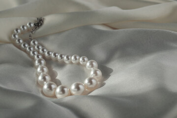 Beautiful pearl necklace on white silk, closeup. Space for text