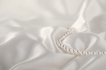 Beautiful pearl necklace on white silk, closeup. Space for text