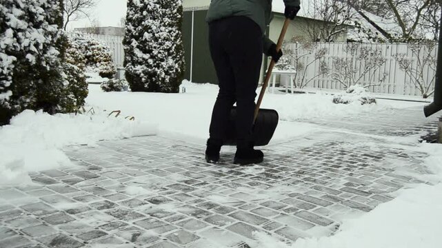 Woman cleaning her snowed back yard with plastic shovel. Winter concept.