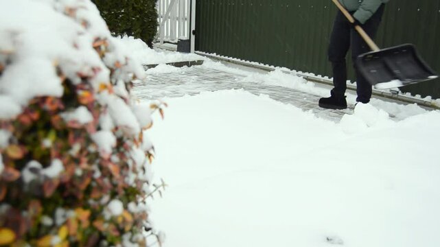 Woman cleaning her snowed back yard with plastic shovel. Winter concept.