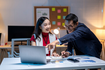 Asian business people having fun while working late night in office using laptop computer