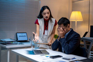 Businesswoman scolding businessman covering his face at office desk at night