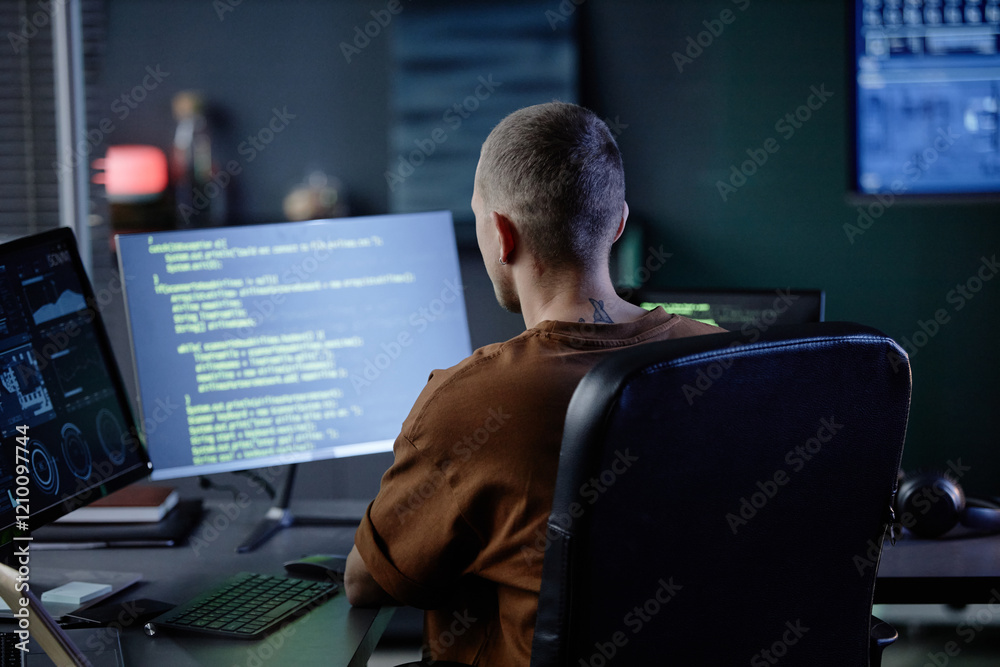 Poster rear view of male software developer working at desk with multiple computer screens writing code in 