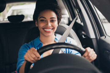 Smiling young woman driving a car in the city on a sunny day, enjoying the journey and feeling confident behind the wheel