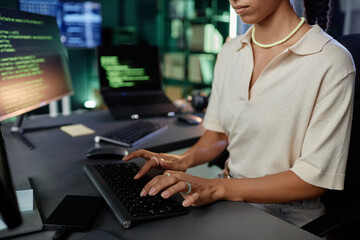 Cropped shot of female IT programmer typing source codes on computer keyboard sitting at workstation with several devices while working at office workplace
