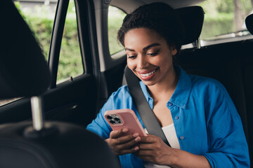 Young woman enjoying a taxi ride, smiling at her phone while seated in the backseat of a...