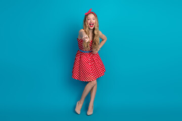 Happy woman in red polka dot dress pointing with hand against blue background