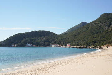 Beautiful beach with a blue ocean and mountains in the background. The beach is empty and the sky is clear Portinho da Arrábida beach, Setúbal, Portugal.