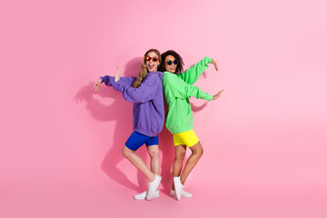 Young friends posing playfully in stylish colorful outfits against a vibrant pink background