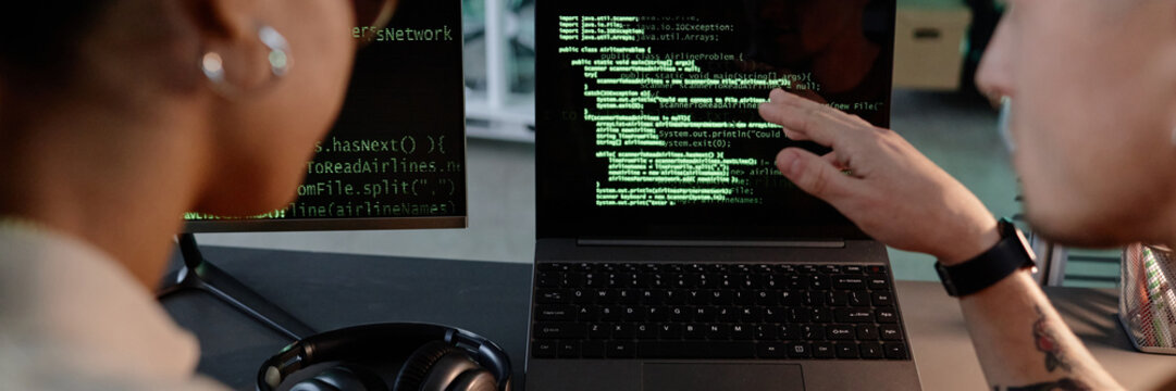 Website header shot of unrecognizable male and female colleagues pointing at laptop screen discussing code debugging while working collaboratively in office