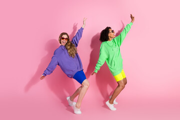 Excited women dancing in sporty colorful clothes against a pink background
