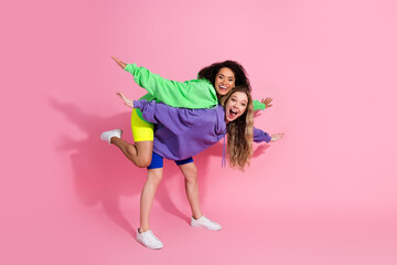 Two cheerful young women in colorful hoodies posing playfully against a vibrant pink backdrop, embodying friendship and joy