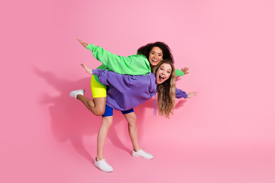 Two cheerful young women in colorful hoodies posing playfully against a vibrant pink backdrop, embodying friendship and joy - Powered by Adobe
