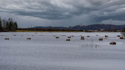 Flooded Field with Hay Bales Floating in Water on a Cloudy Day. Hay Bales in a Submerged Meadow During Seasonal Flooding.