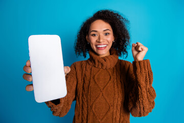Enthusiastic woman presenting smartphone with cheerful gesture against a bright background