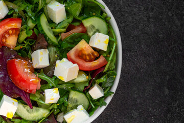Fresh salad with tomatoes, feta and arugula on a dark background, top view close-up