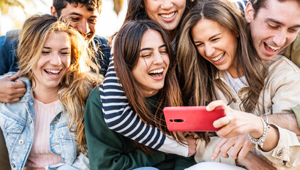Group of young people using smart mobile phone outdoors - Happy friends with smartphone laughing together watching funny video on social media platform - Tech and modern life style concept