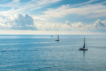 Calm blue ocean surface with a few sailboats in the distance and a sunny sky above, waves, horizon, sea