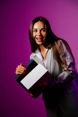 Confident woman holding a book while smiling against a vibrant purple background