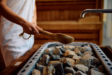 Close up of woman pouring water on hot rocks in sauna.