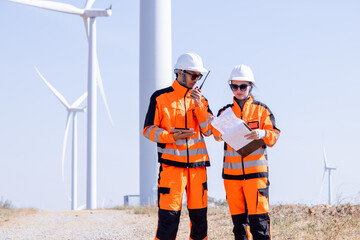 Team of male and female engineers discuss for maintenance of wind turbines at windmill field farm. Group of engineers workers working at wind turbines farm. Alternative energy, environmental friendly.
