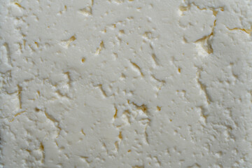 Texture and background of a piece of fresh white cottage cheese, closeup, top view. Homemade white cheese from cow's milk