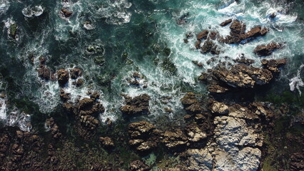 A breathtaking aerial drone view of the rugged rocks and tranquil sea off Asilomar Beach, nestled...
