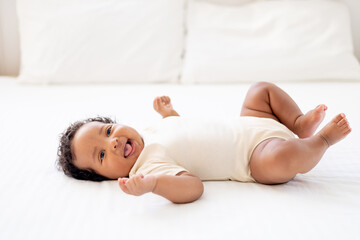a close-up portrait of a small African-American baby girl in a white bodysuit on a cotton bed at...