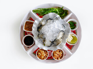 Fresh oysters on the half shell on ice with lime wedges and other side dishes, spicy Thai style, seafood meal from the sea, local food