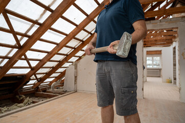 A handyman with a hammer  during the renovation of the attic in a private house.