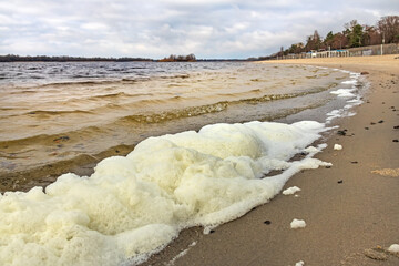 White foam on the bank of the Dnieper river (Dnipro) in Kremenchuk city, cloudy windy day
