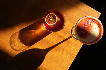 Two cocktail glasses with a slice of dry orange and ice cube on a wooden table.