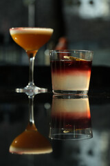 Two cocktail glasses with a slice of dry orange and ice cube on a wooden table.
