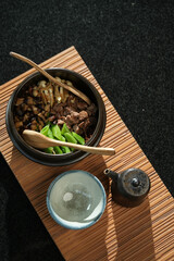Japanese food, Fried beef with mushrooms and vegetables in a bowl on a bamboo mat