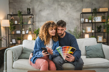 Couple hug while selecting vibrant color swatches and use mobile phone