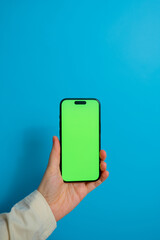 Close-up of female hand using smartphone isolated on blue background. Female hands showing blank green screen of modern smartphone.
