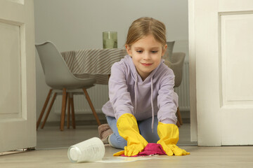 Little girl cleaning spilled milk on the floor