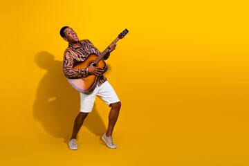 Cheerful young man playing guitar enthusiastically against bright yellow background, enjoying music...