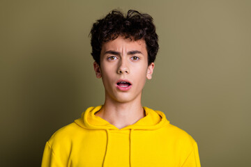 Surprised teenage boy in a bright yellow hoodie posing with a khaki background