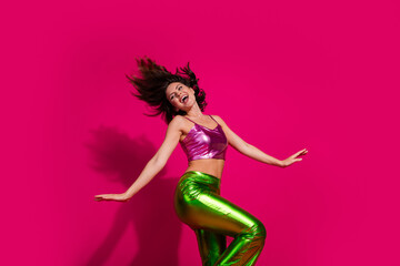 Young woman dancing energetically in vibrant pink and green outfit against bright magenta background