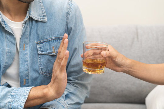 Alcoholism, depressed asian young man refuse, push out alcoholic beverage glass, drink whiskey, sitting alone at night. Treatment of alcohol addiction, having suffer abuse problem alcoholism concept.