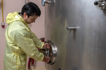 Professional male Caucasian wine maker working with stainless barrel in fermentation room