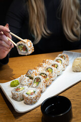 A person holding a sushi roll with chopsticks with sushi set