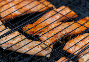 Grilled trout fish sizzling over an open flame in a rustic outdoor setting at twilight