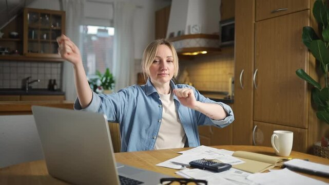 A woman sits at a table in the kitchen, happy from successfully completed financial work. There are papers, a laptop and a calculator on the table. success in financial management.