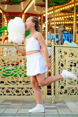 Obraz premium a child in an amusement and amusement park, a happy girl eating cotton candy and enjoying the holidays and summer, a child came to ride on a carousel