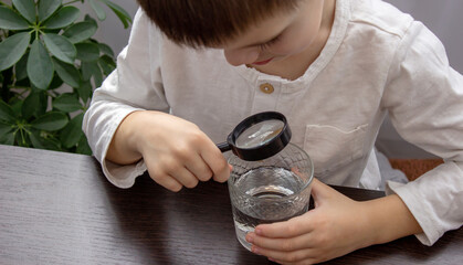 little boy looking at water through a magnifying glass, water analysis.