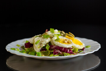 Salad with seeds and vegetables in a plate, isolated on a black background