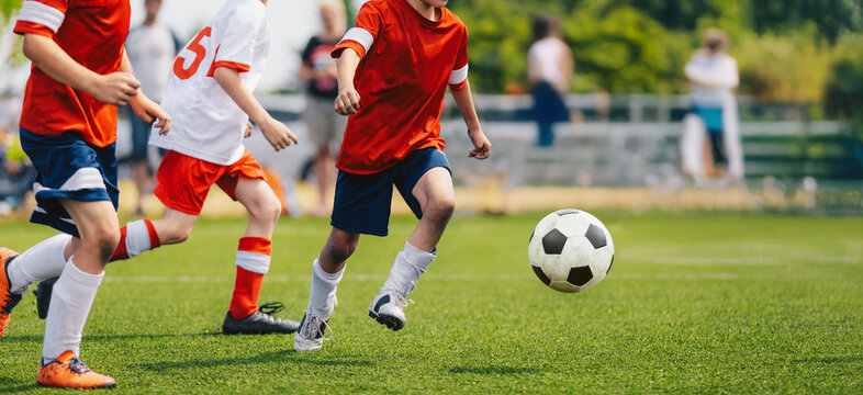 Boys play football game during youth football league. Players in speed duel. Kids have fun in sports match. Soccer boys kicking a ball on grass turf. Kids in red and white soccer jersey shirts